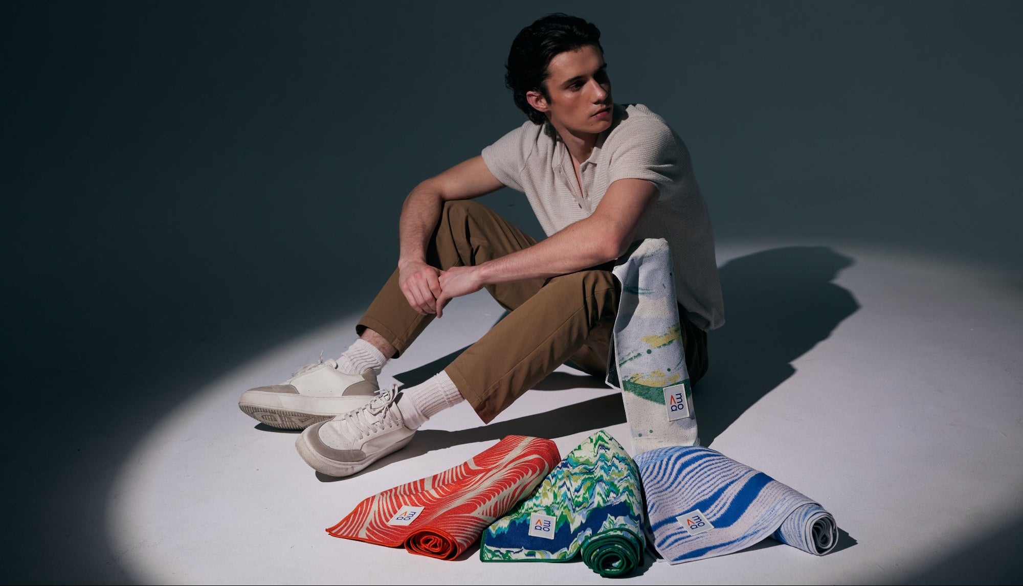 Man sitting on a white surface with colorful towels, against a dark background