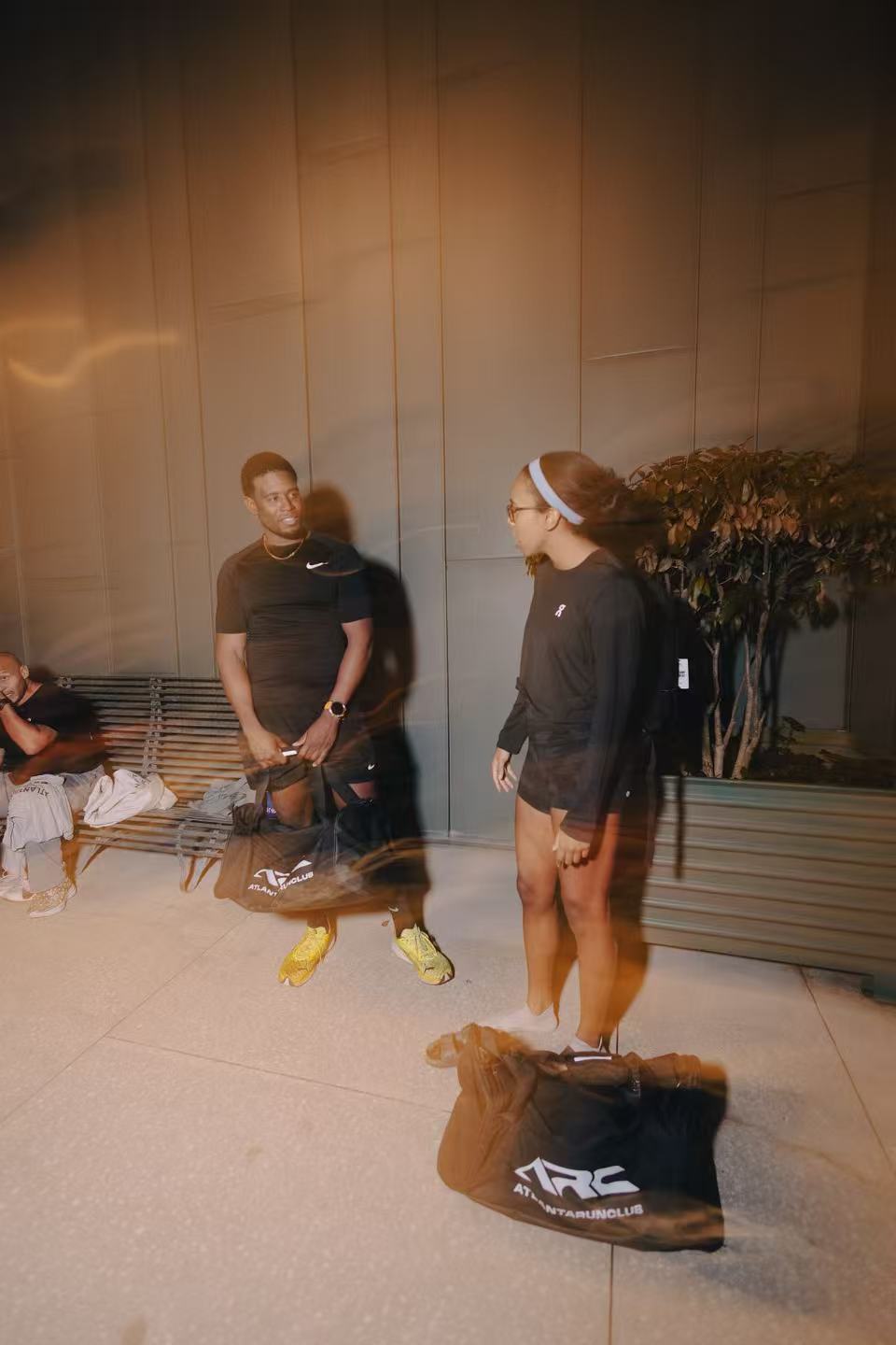 Two people standing in a room with a plant and bench in the background