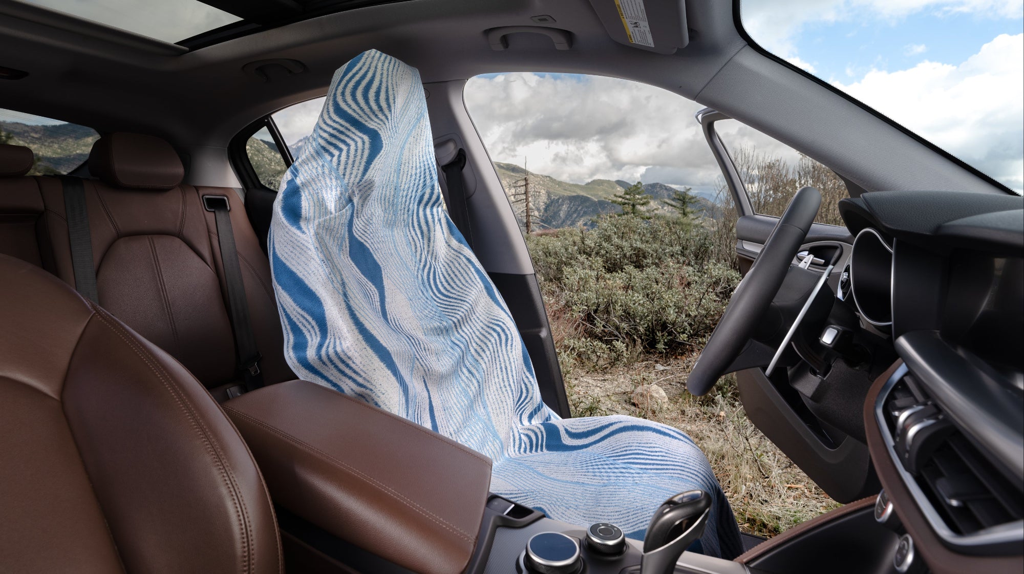Car interior with mova patterned seat towel on the driver's seat, showing a scenic view through the windows.