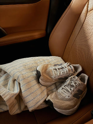 Pair of beige sneakers on a brown car seat with a striped towel.