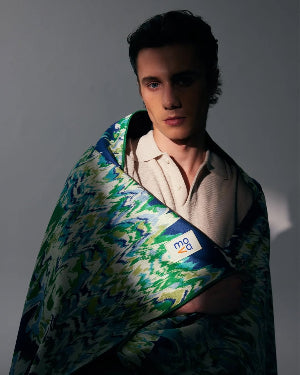 Person wrapped in a colorful patterned blanket with a visible brand logo on a gray background