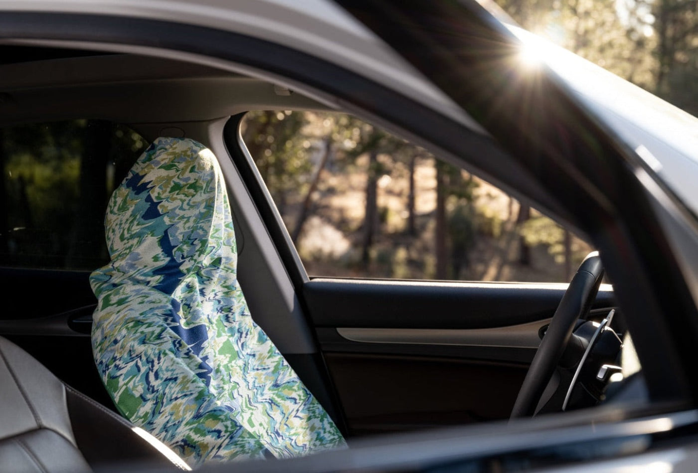 Car interior with a floral-patterned car seat cover towel on the driver's seat, sunlit through the window.