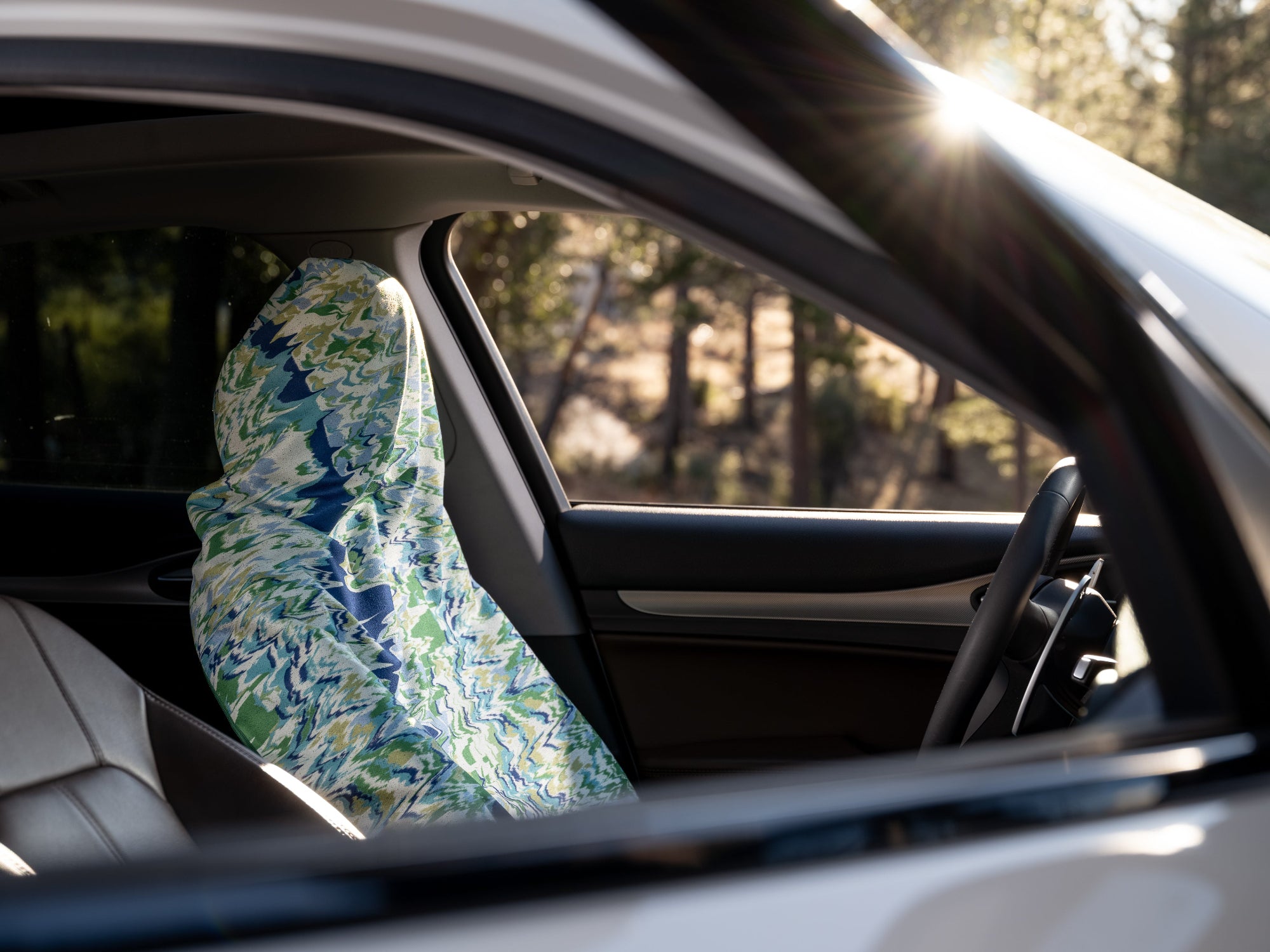 Car interior with a floral-patterned seat cover on the driver's seat, sunlit through the window.