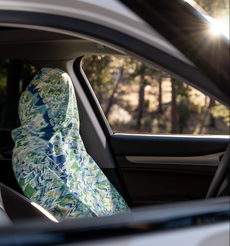 Car interior with a floral-patterned seat cover on the driver's seat, sunlit through the window.