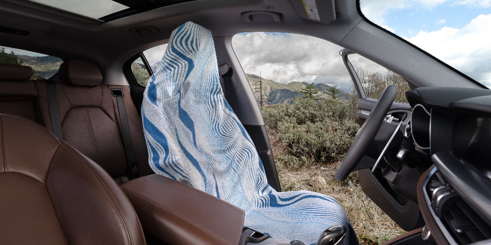 Car interior with a patterned cover over the front seat, showing a scenic view through the windows.