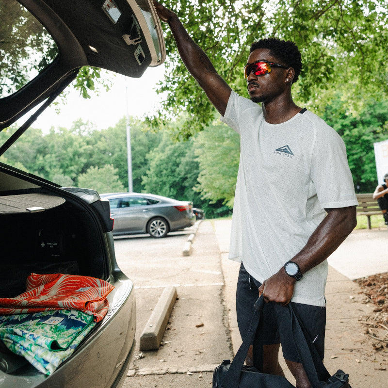 Man loading a suitcase into a car trunk with trees in the background