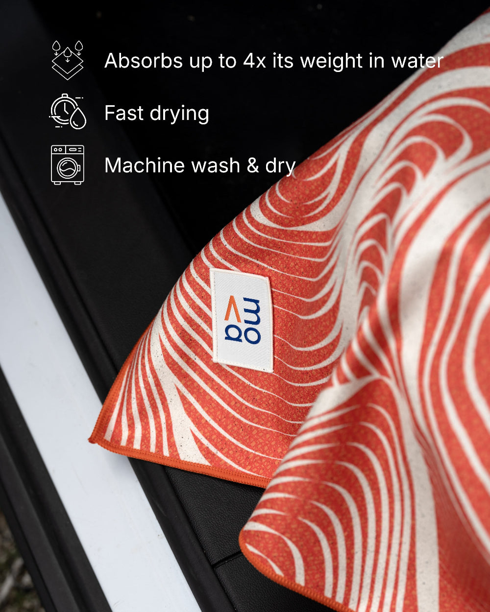 Red and white patterned towel with a brand logo, hanging on a black surface.