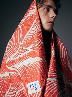 Person wrapped in a red and white patterned towel with a visible brand logo on a dark background